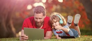 Father and son lying on the grass with a laptop